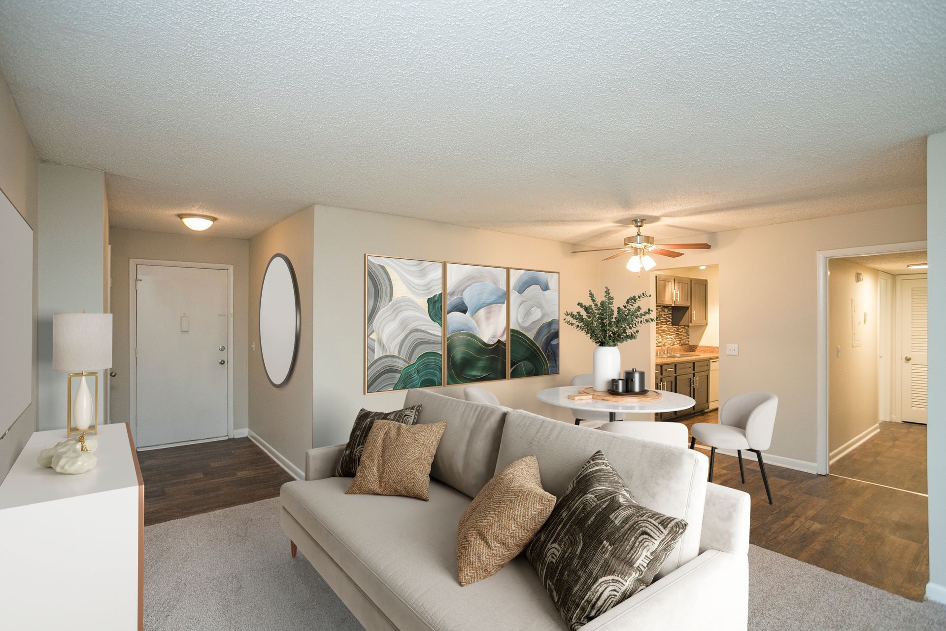 A modern, neutrally-decorated living room with a cream sofa, triptych art on the wall, and a view into a dining area.