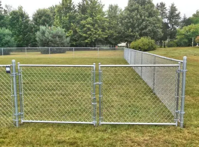 A chain link fence with a gate in the middle of a grassy field.