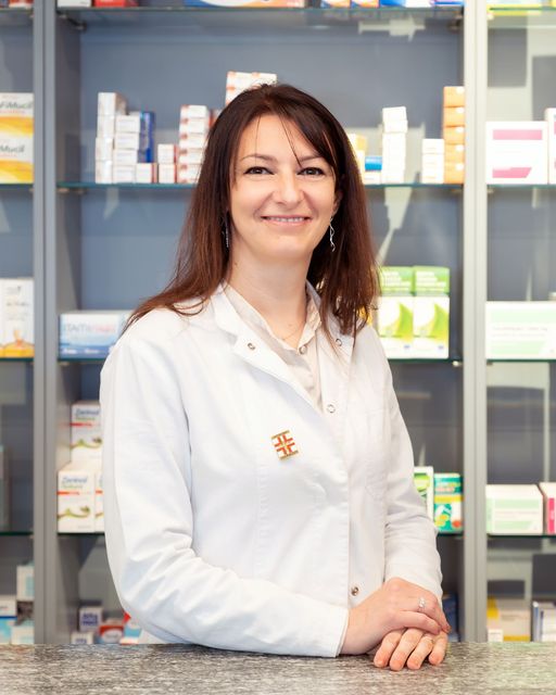 Una donna con un camice bianco è seduta al bancone di una farmacia.