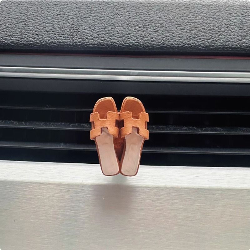 A pair of sandals are hanging from a car air vent.