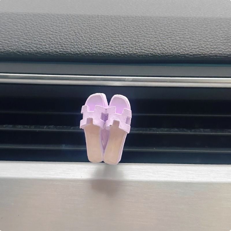 A pair of pink sandals are hanging from a car air vent.