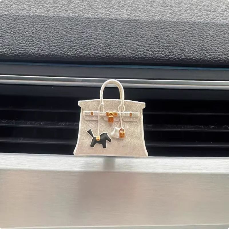 A white purse with a horse on it is hanging from the air vent of a car.