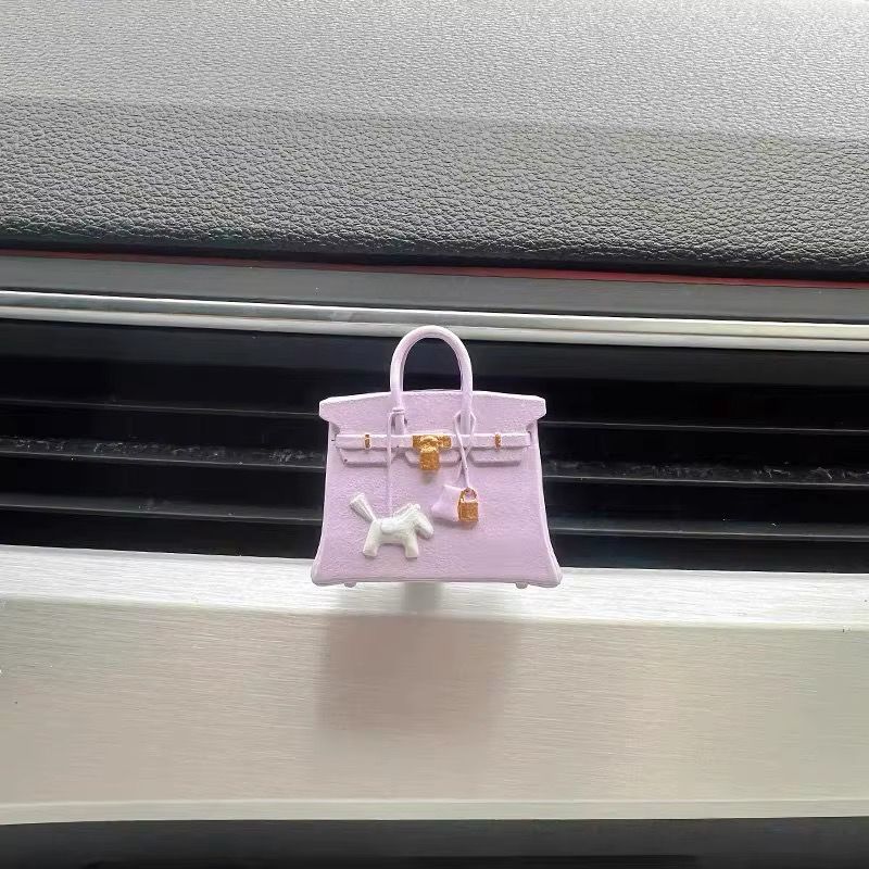 A purple purse with a dog on it is hanging from a car air vent.