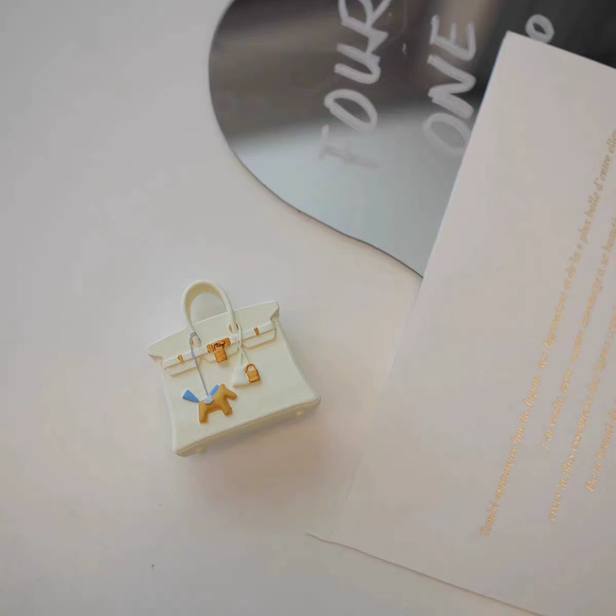 A small white purse is sitting on top of a piece of paper next to a mirror.