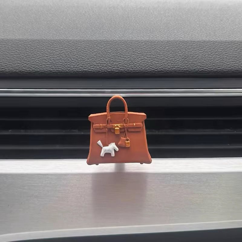 A brown purse with a white horse on it is hanging from the grille of a car.