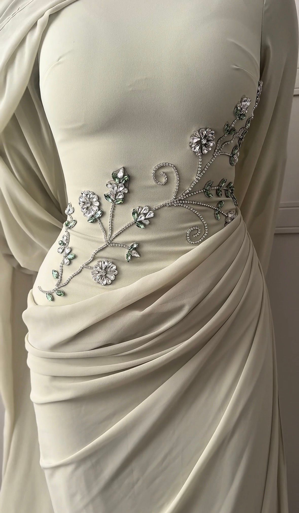 Beige draped gown with jeweled floral embellishment on the side and shoulder overlay