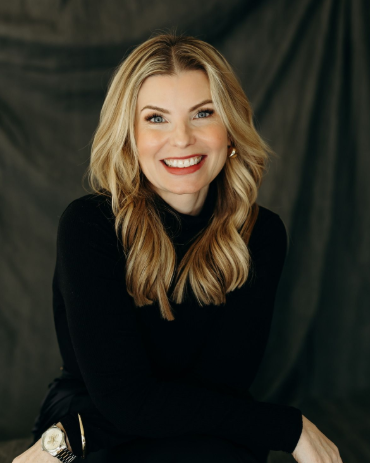 Smiling blonde woman in a black top posing against a dark backdrop
