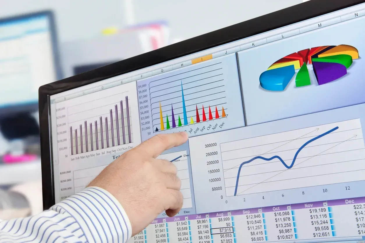 Hand pointing at a computer screen with colorful charts and graphs in an office setting