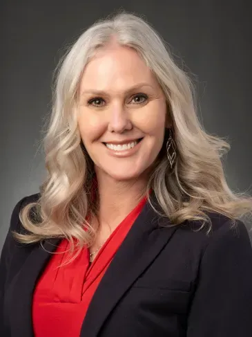 Smiling woman in a red blouse and dark blazer against a gray background