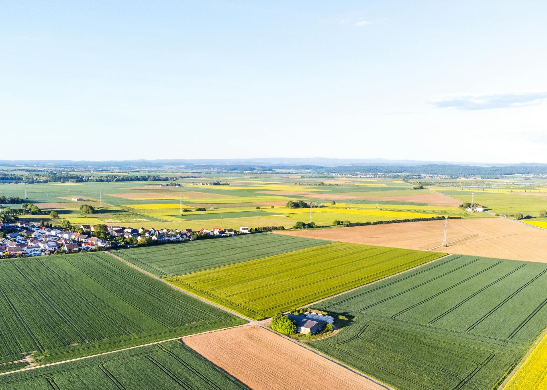 Aerial view of patchwork farmland, a small village, and a bright blue sky on the horizon.