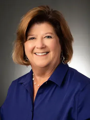 Smiling woman in a blue blouse against a gray studio backdrop