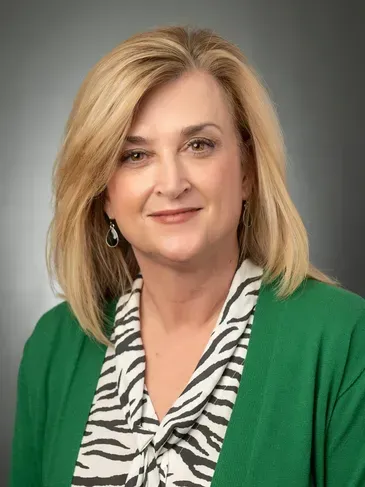 Portrait of a smiling woman in a green cardigan and zebra-print blouse against a gray background