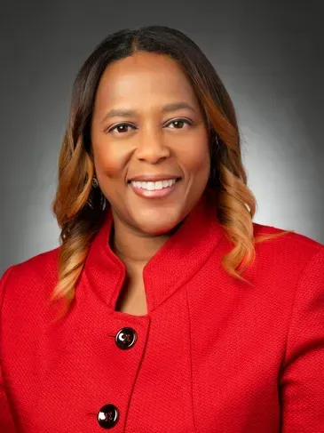 Smiling person in a bright red blazer against a gray studio background