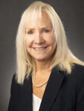 Smiling blonde woman in a black blazer and white top against a gray background