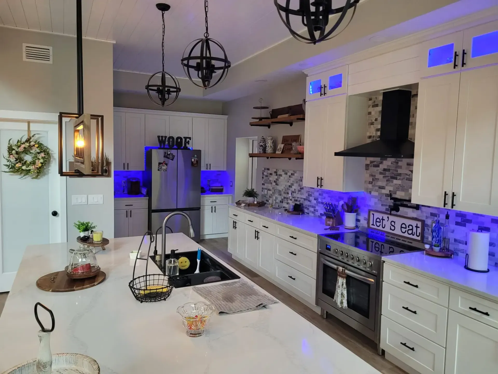 Modern kitchen with white cabinets, marble island, blue accent lighting, and hanging black pendant lights, customized by All Pro Builders