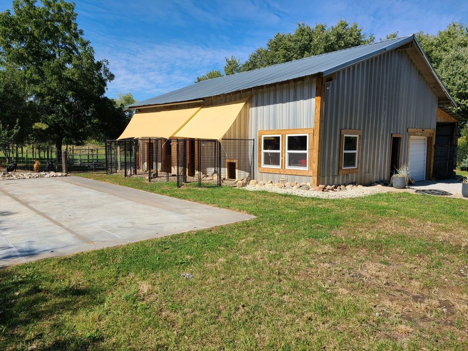 Rustic barn with tan awning and metal roof beside a paved lot on a sunny day