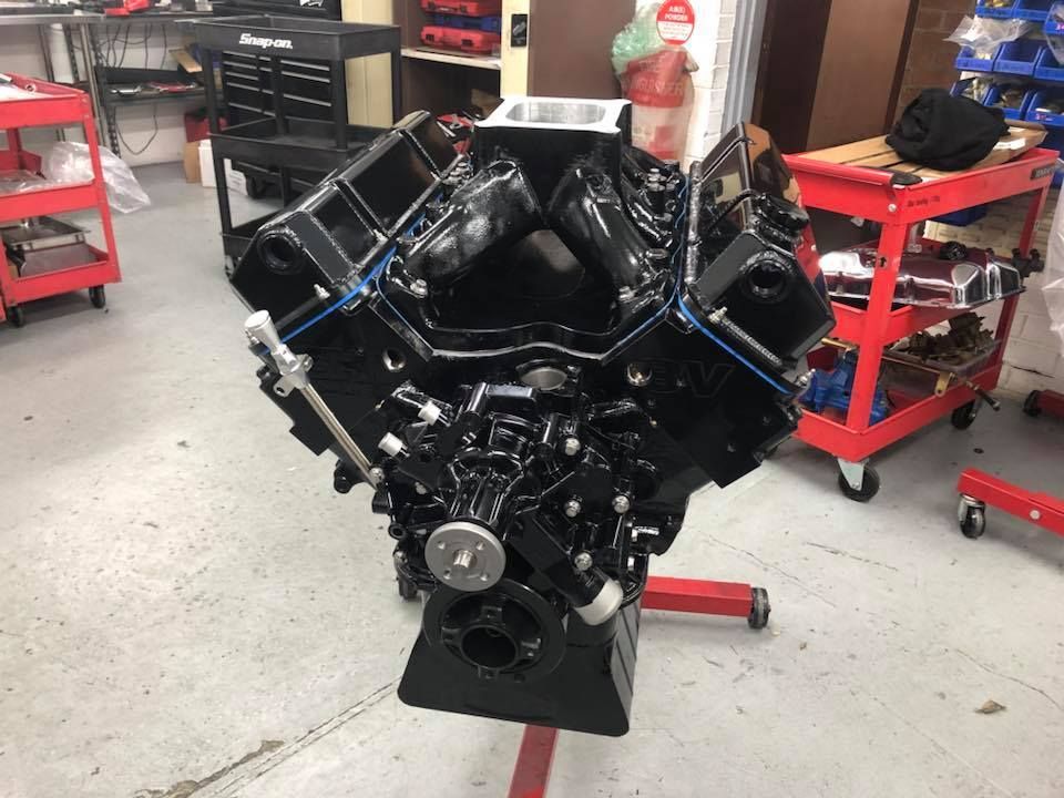 A black engine is sitting on a red stand in a garage.