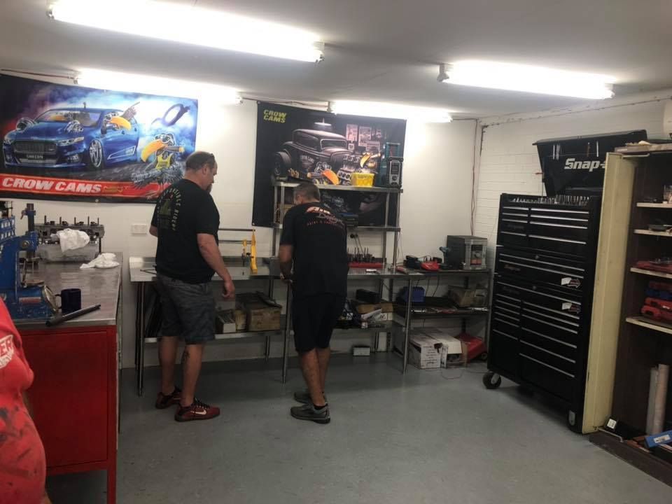 Two men are standing in a garage working on a car.