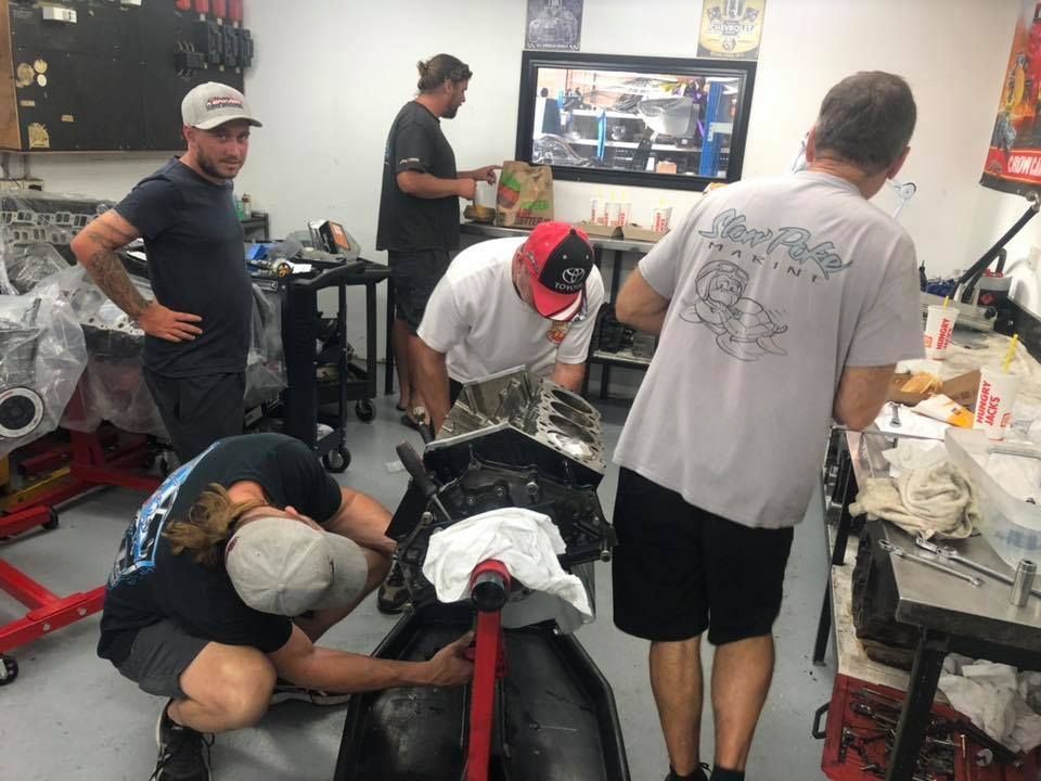 A group of men are working on a car engine in a garage.