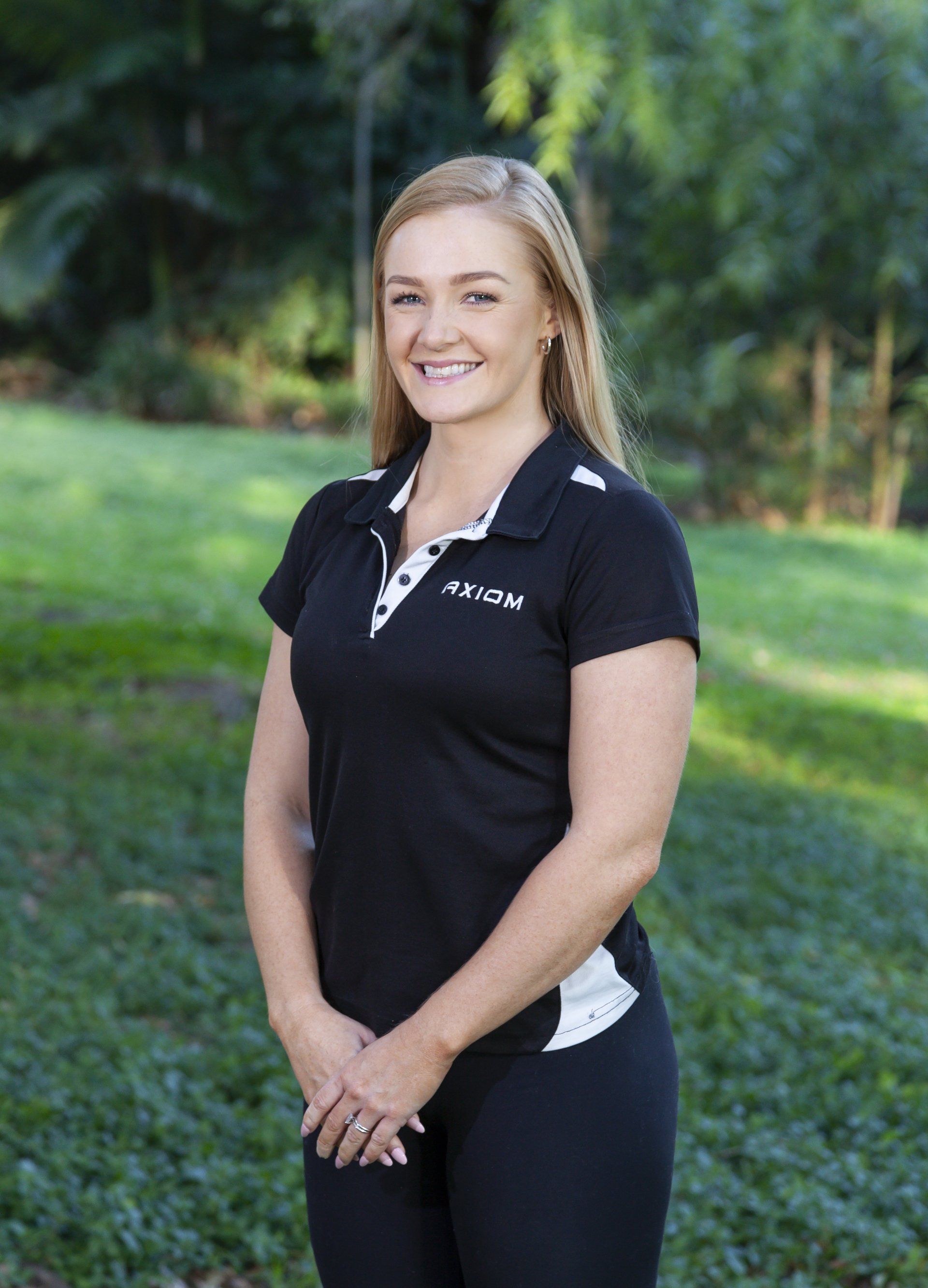Woman in a black polo shirt, smiling, standing in a park.