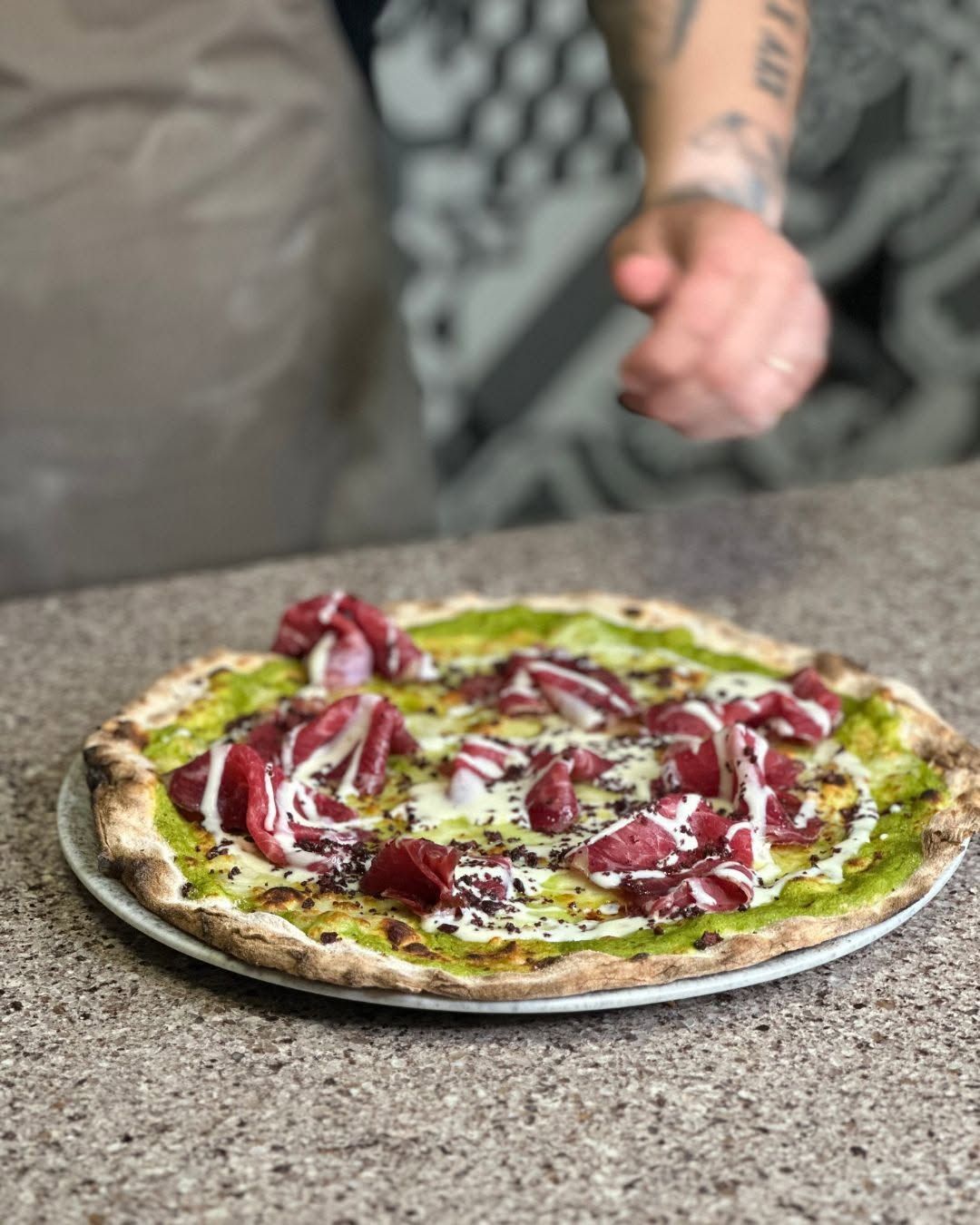 Pizza condita con verdure, cipolle rosse e glassa bianca, servita su un piano di lavoro in pietra.