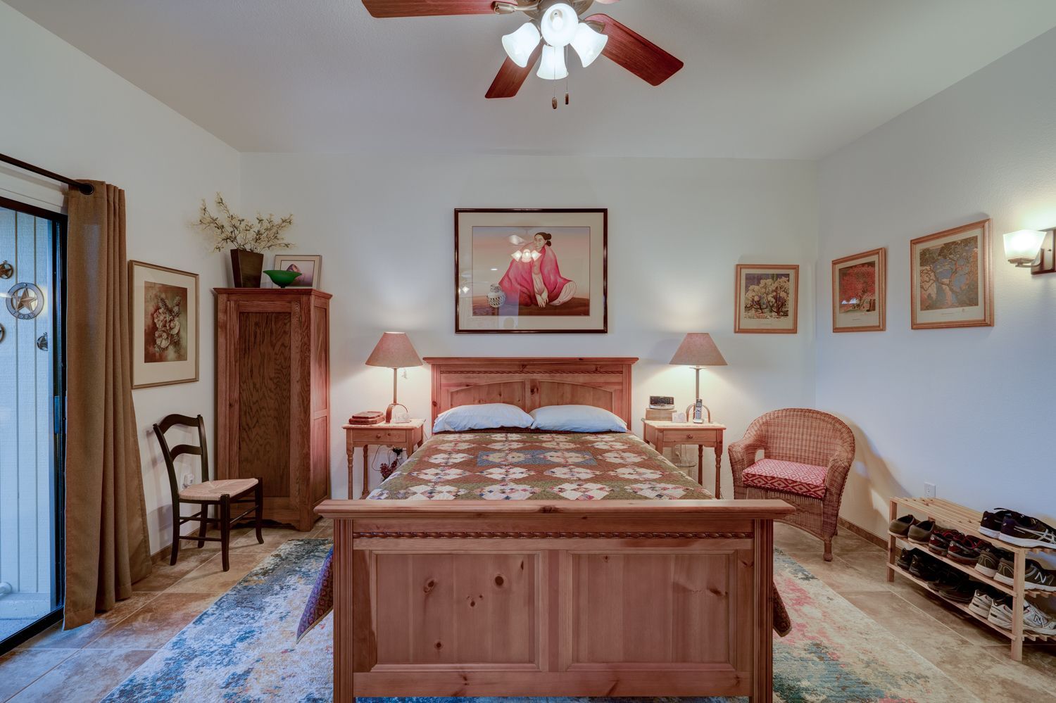 Bedroom with a wooden bed, dresser, and artwork on cream-colored walls. A ceiling fan is overhead.