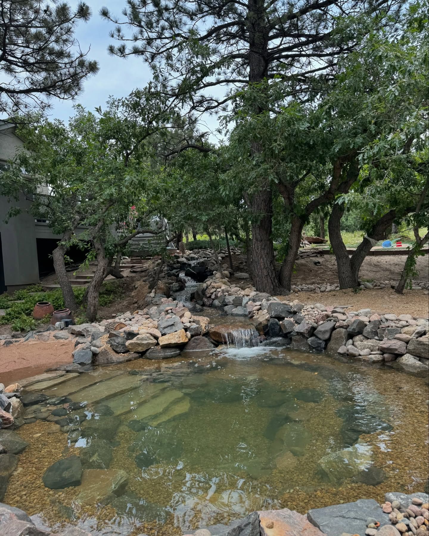 Water pond with small waterfall, surrounded by trees and rocks.