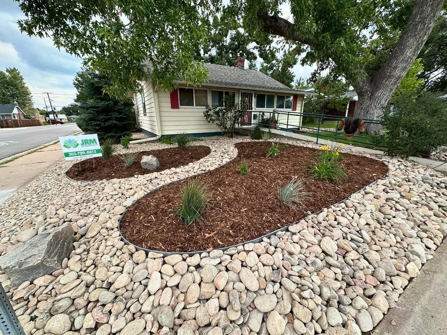 Small house with rock and mulch landscaping; tree provides shade.