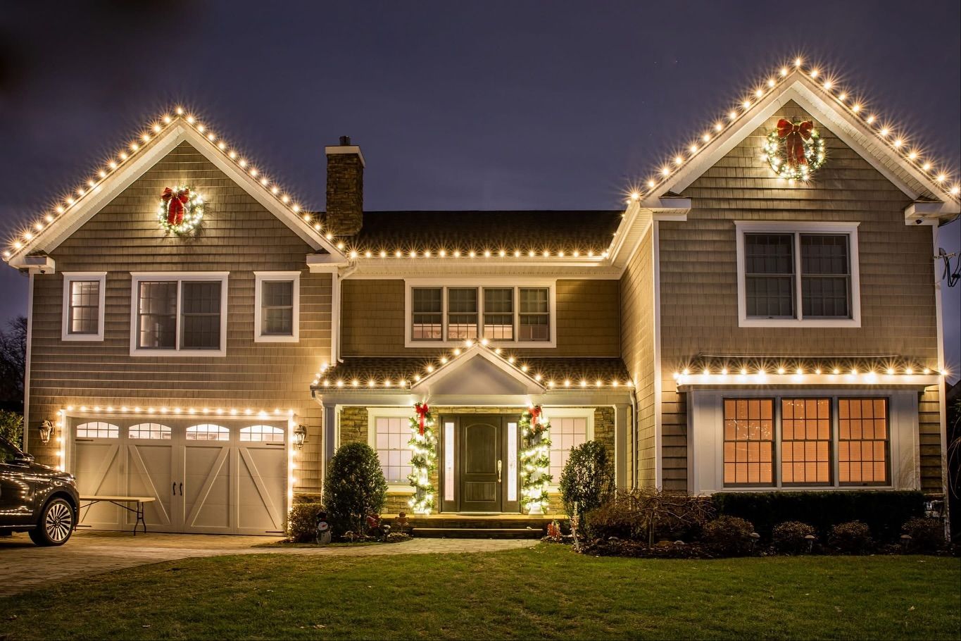 House decorated with white Christmas lights and wreaths; garage door, front door, and windows.