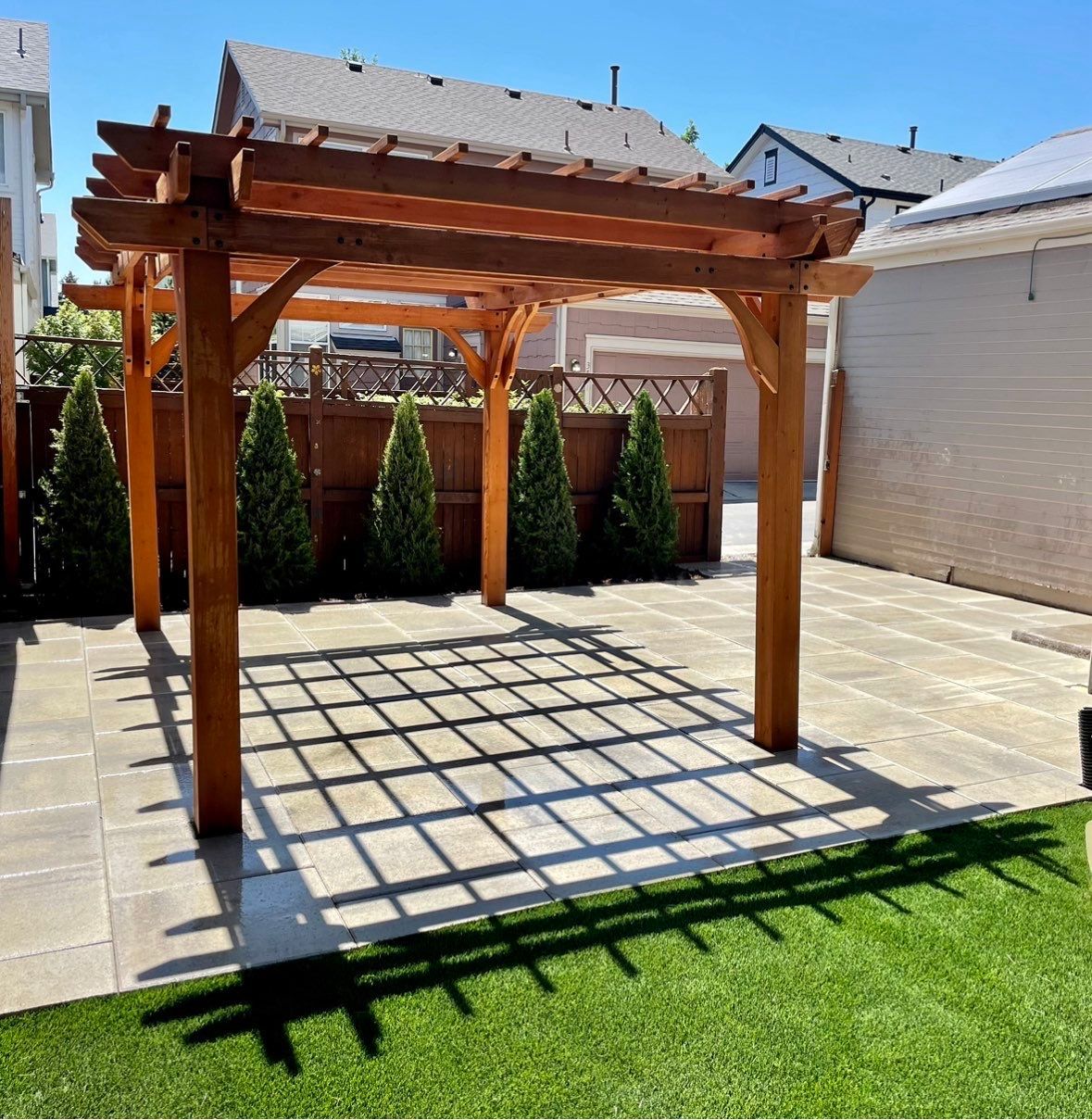 Wooden pergola structure over a concrete patio in a backyard setting.