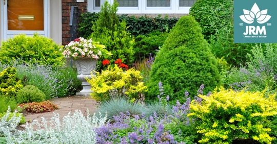 Colorful, vibrant garden bed in front of a house, featuring various shrubs and flowers.
