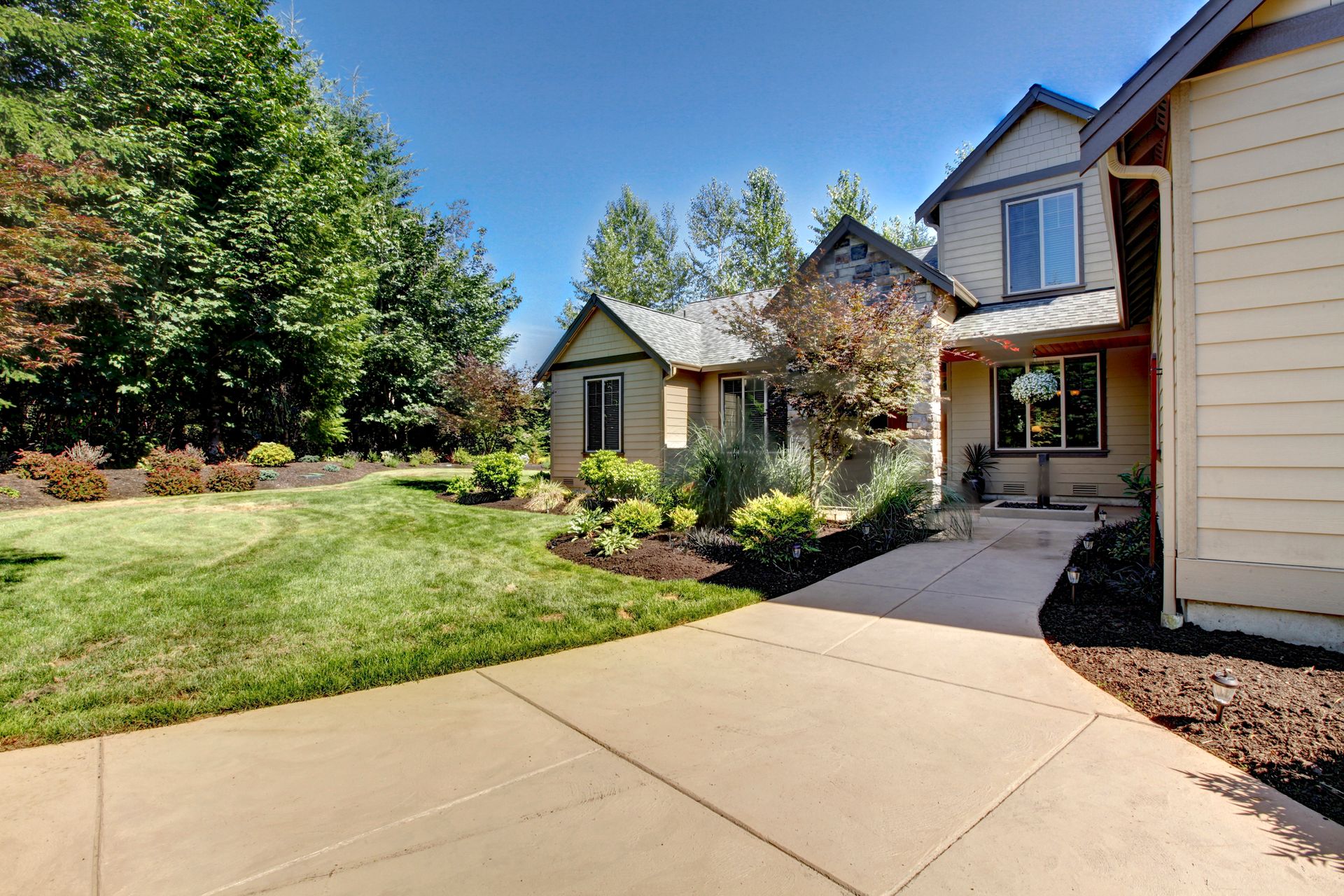 Suburban house exterior with driveway, front lawn, and landscaped yard on a sunny day