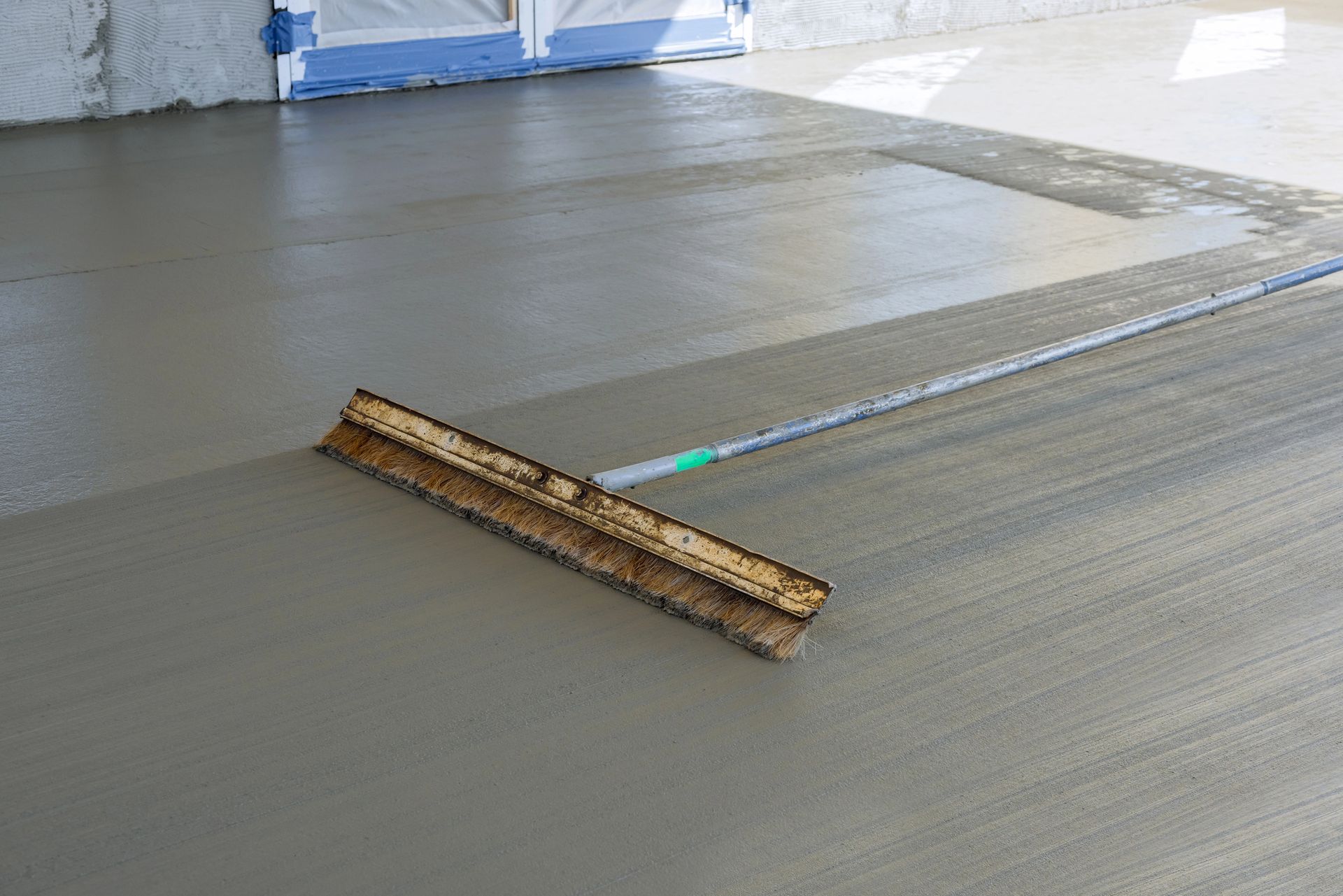 Freshly poured concrete floor being smoothed with a long straightedge tool