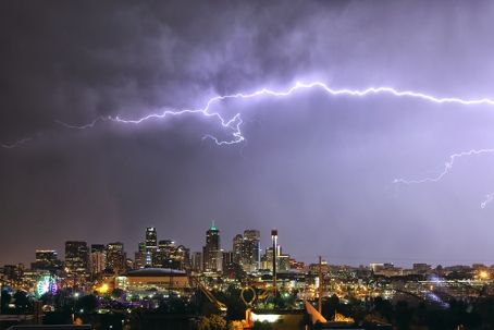Lightning illuminates a city skyline at night with dark clouds.