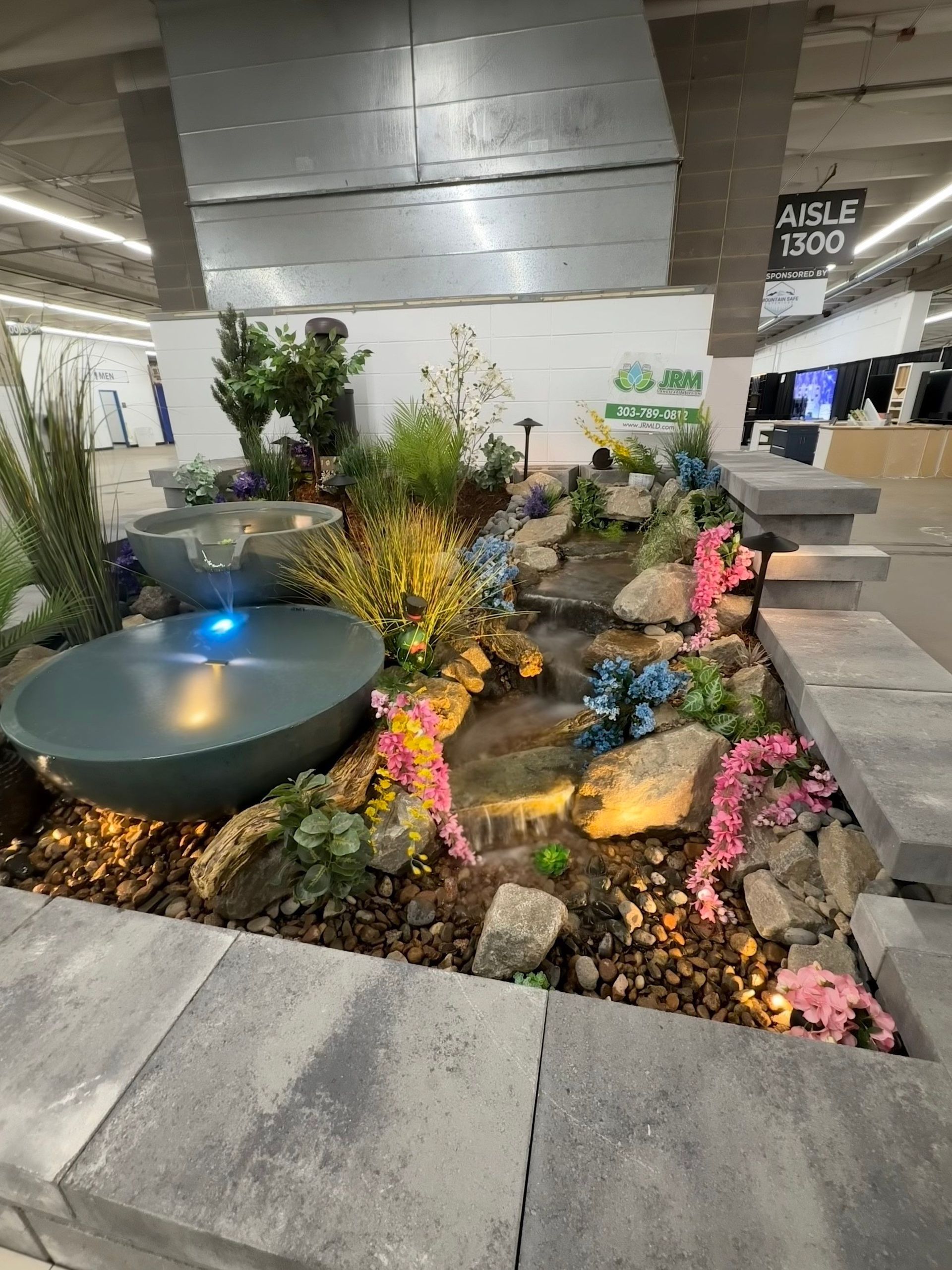 Indoor display featuring a cascading water fountain with colorful flowers and greenery.