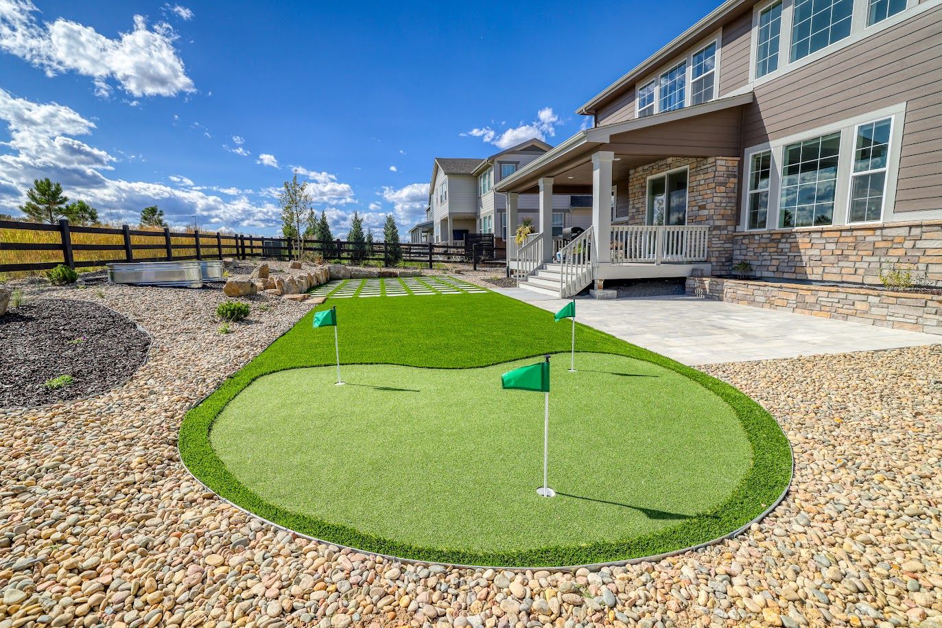 Backyard putting green with flags, surrounded by gravel, near a house.