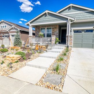 Curb appeal of a house with stone and stucco facade, concrete walkway and driveway, and rock landscaping under a blue sky.