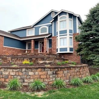 Two-story house with blue siding, brick accents, and a tiered retaining wall in the front yard.