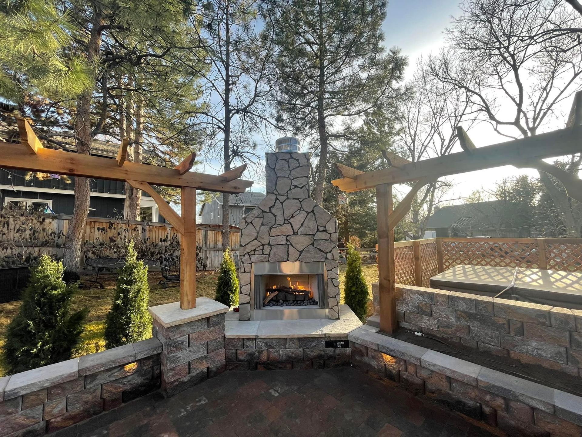 Black and wood-toned pergola with wooden slats, seen from below against a cloudy sky and leafy trees.
