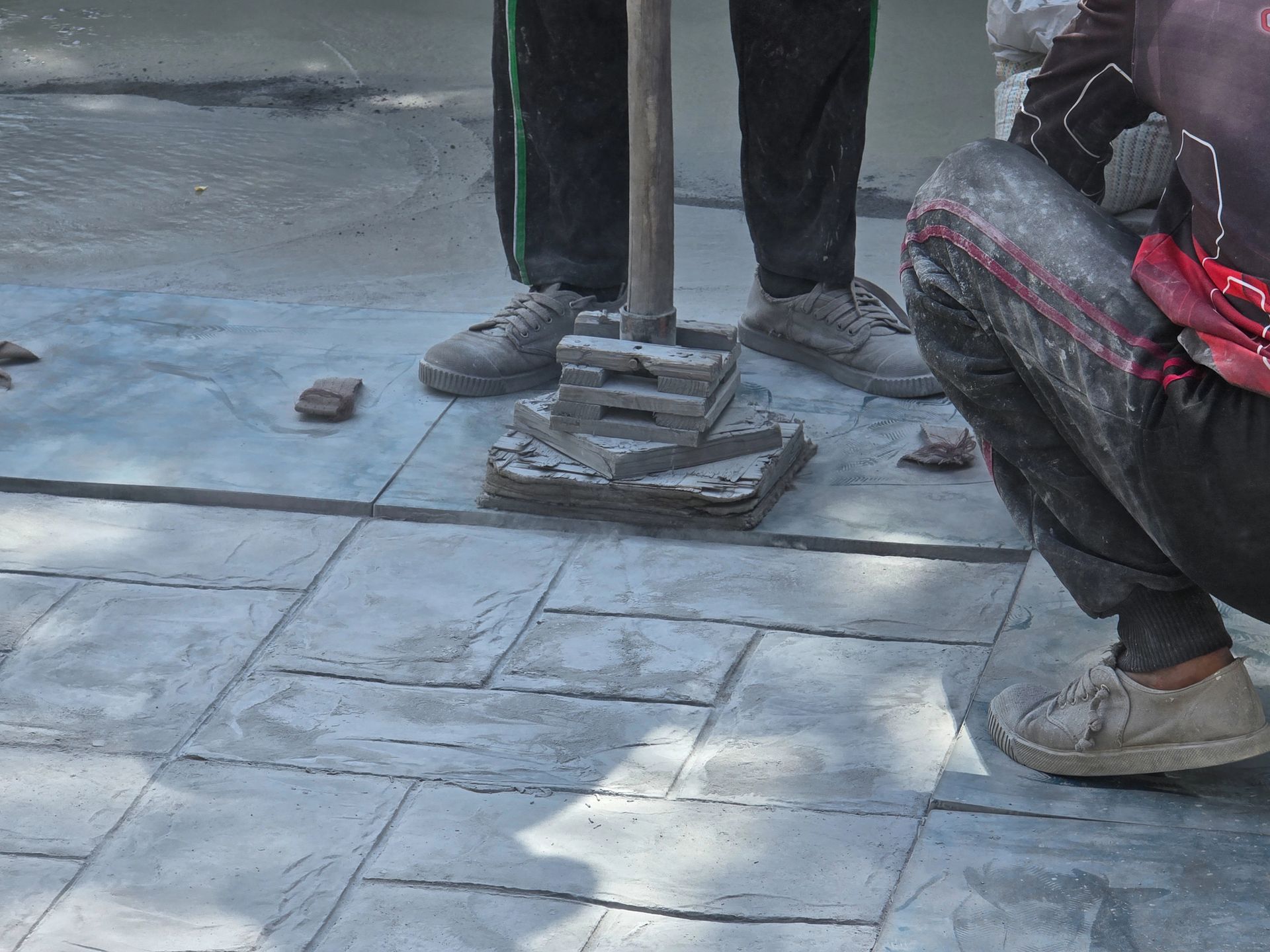 Workers’ legs around a tiled floor, with a small pile of bricks or concrete pieces in the center