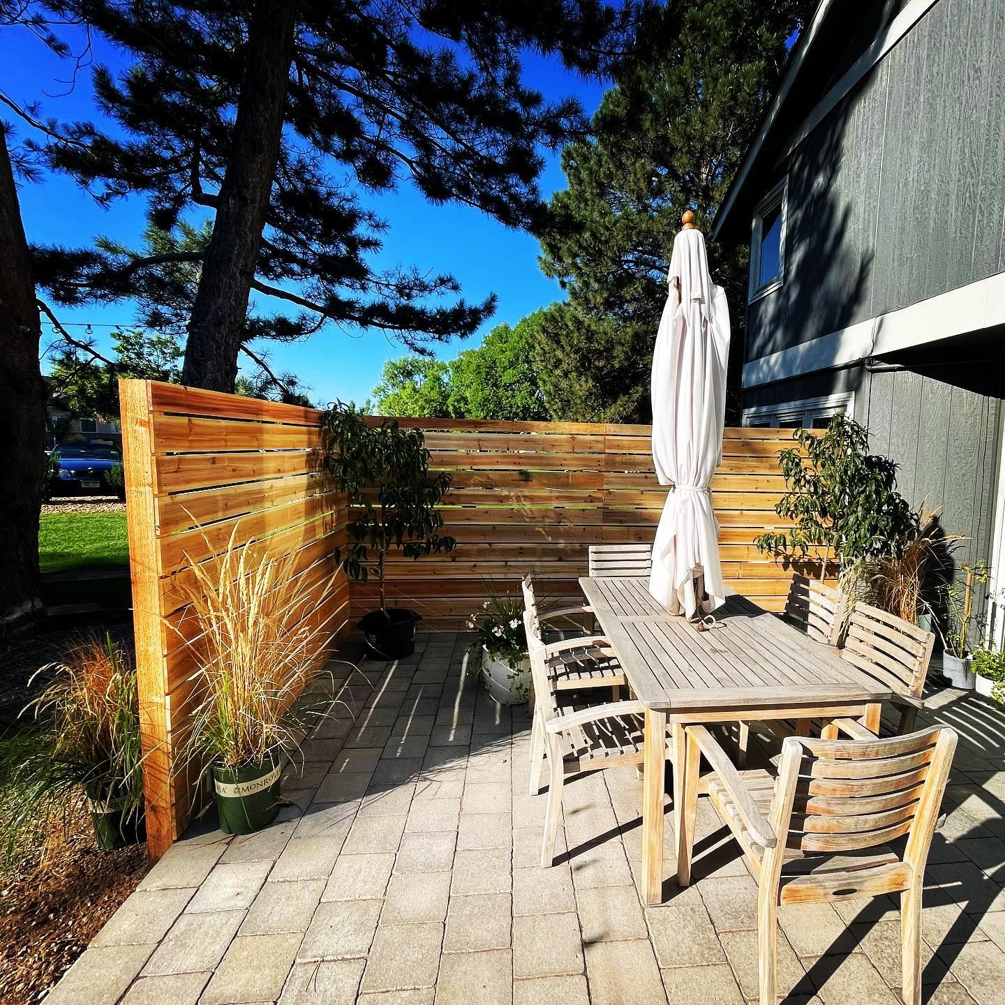 Wooden patio with table, chairs, and umbrella next to a building and wooden fence.