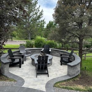 Outdoor fire pit with seating. Paver patio, stone walls, and Adirondack chairs around a fire pit with trees in the background.
