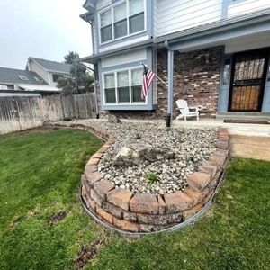 Front yard with brick border, rock bed, and two-story house with an American flag.