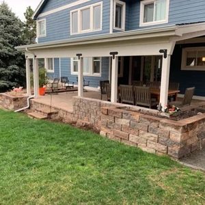 Blue house with covered patio, stone retaining walls, and green grass.