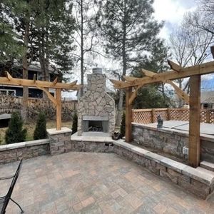 Stone fireplace with wooden pergolas in a paved outdoor patio setting.