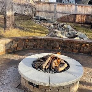 Fire pit in a backyard setting with a stone wall and small waterfall.