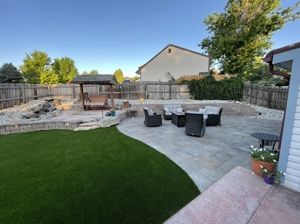 Backyard patio with seating, artificial lawn, and a wooden swing set against a wooden fence.