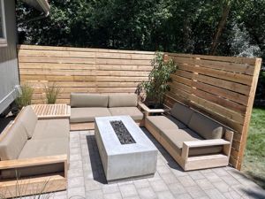 Outdoor seating area with light-brown couches, concrete fire pit, and wooden fence.