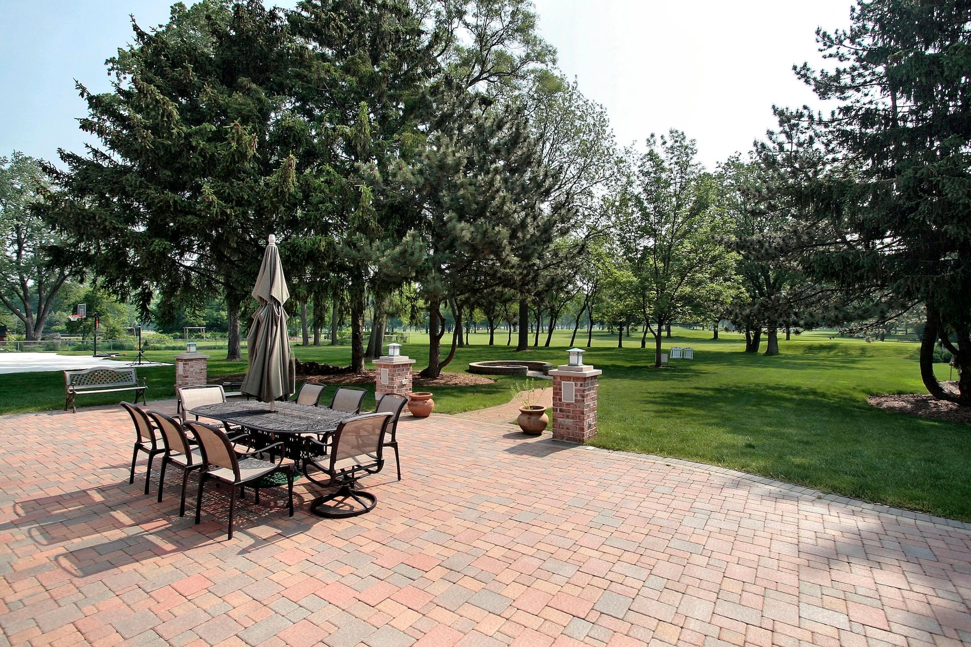 Patio with brick pavers, table, chairs, umbrella, and trees in a grassy yard.