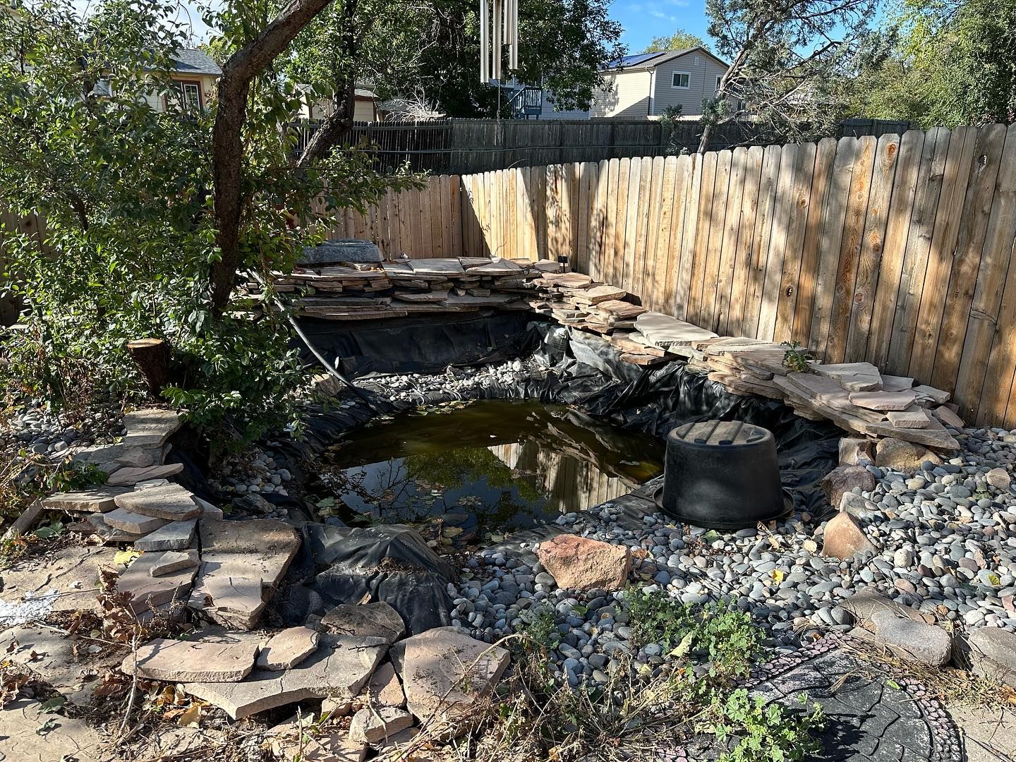Backyard pond surrounded by rocks and a wooden fence. Overcast day.